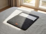 Soft grey laptop cover lying on a white bed sheet.