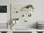 Pegboard wall organizer above a white desk holding stationery, photos, and plants.