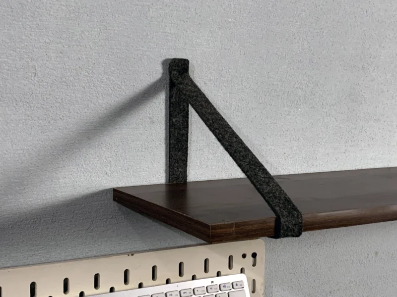 Detail shot of felt strap bracket holding a dark wood shelf board.