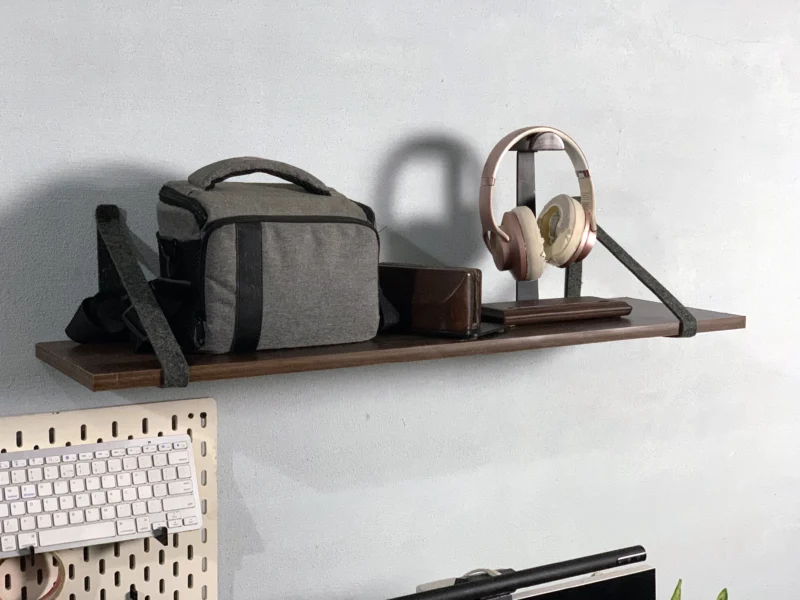 Floating shelf with felt straps holding camera bag and headphones above a desk.