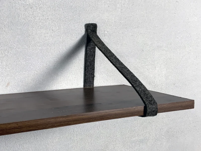 Detail shot of felt strap bracket holding a dark wood shelf board.